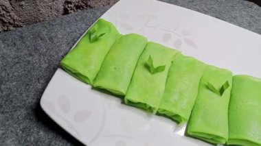 Endonezya yemeği. Dadar Gulung güzel bir tabakta sunuluyor. Arkaplan olarak tuğla bir duvar var. Buğday unu, hindistan cevizi, palmiye şekeri ve pandan aromalı..