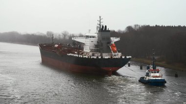 Kiel Canal, Germany - 01 11 2023: Oil tanker sailing along the shipping lane with the assistance of the tug boat