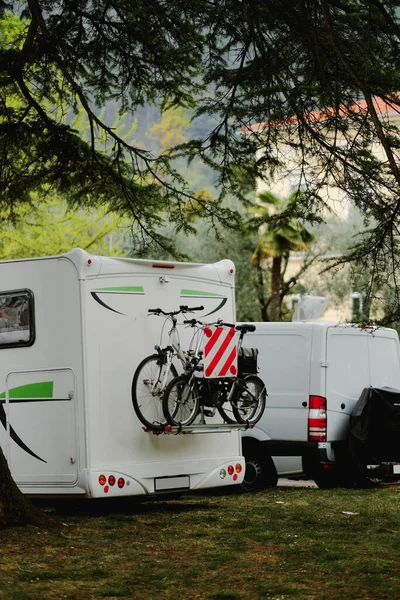 A white van is parked next to a white travel van with two bikes safely secured from the back side.