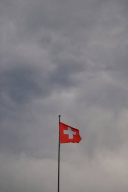 İsviçre bayrağı bulutlu ve kasvetli gökyüzünün altında dalgalanıyor.