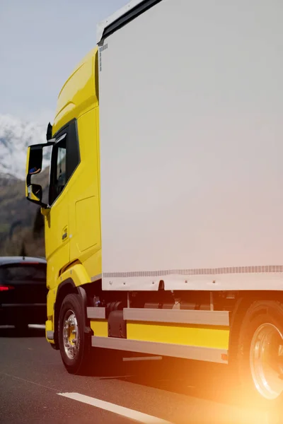 Side view of the long range truck on the European highway. Express delivery and shipping of the goods. Door to door logistics. Semi truck with a yellow cabin and white trailer. Customers support