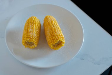 Beyaz masadaki tabakta iki mısır filizi.