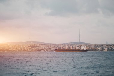 Uluslararası ticaret yapan bir kargo gemisi arka planda büyük bir şehirle uluslararası seyir kanalında yol alırken...