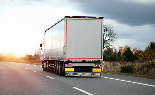 Modern white semi-trailer trucks on the highway driving in the right lane. Commercial vehicle for shipping and post delivery. Shipping of the goods on land with a door-to-door delivery process.