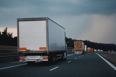 Otoyolda sağ şeritten giden modern yarı karavan kamyonları. Nakliye ve posta teslimatı için ticari araç. Malların kapı kapı dolaşımı.