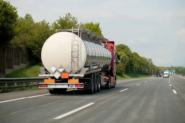 stock image Petrol truck on highway hauling fossil oil refinery products. Fuel delivery transportation. Aviation fuel transportation. Compressed gas carrier truck rear view on a highway. Dairy products carrier.