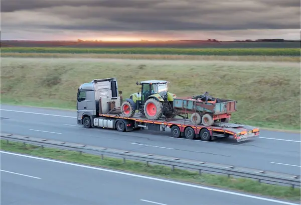 stock image Heavy-Duty Truck Transporting Agricultural Farm Tractor on Intercity Highway