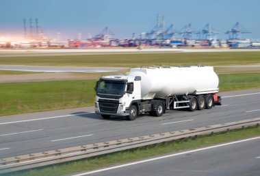 Road Fuel Tanker With Rigid Hull Tank And Container Shipping Terminal In The Background