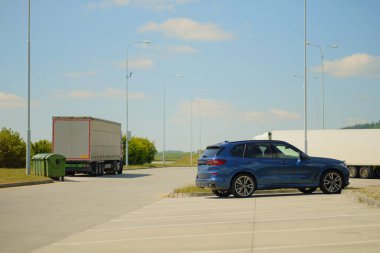 Blue All-Wheel Drive SUV ve Nakliye Truck Sunny Day 'de Modern Otoyol Dinlenme Bölgesi' ne park etti.