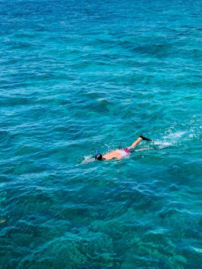 Meksika, Cancun 'un canlı turkuaz sularında bir şnorkelçi yüzer, bir katamarandan görüldüğü gibi. Karayip Denizi güneşin altında parlayarak sakin ve tropik bir manzara yaratır.