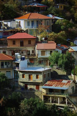 A scenic view of traditional stone houses with red-tiled roofs in Moutoullas village, Cyprus, surrounded by lush greenery and a peaceful mountain backdrop, showcasing Mediterranean charm and heritage. clipart