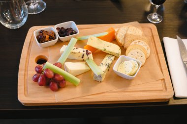 Çeşitli peynir ve krakerlerle dolu ahşap bir tahta. Tahta bir bıçak ve bir şarap kadehiyle masaya konur.