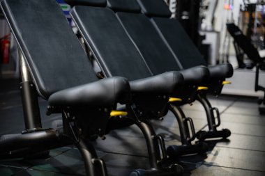 Spor salonunda üç siyah egzersiz sandalyesi sıraya dizildi. Sandalyeler siyah ve sapları sarı.