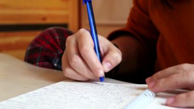 Ev kıyafetleri içinde olan kişi ya kişisel günlüğüne ya da çalışma defterine bir şeyler yazıyordur. Yakın çekim.