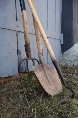 Gri ahşap kapının yanındaki bahçe aletleri..