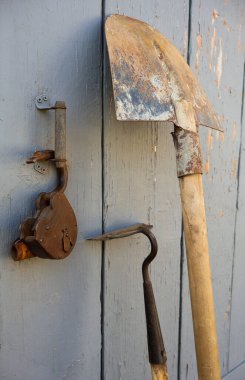 Agricultural implements near a grey wooden gate with a large rusty lock.