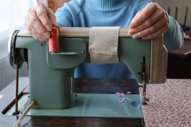 Bir kadın dikiş makinesinde oturur ve pembe iplikleri tutar..
