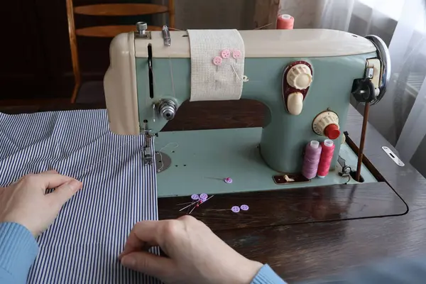 Bir kadın çizgili kumaşlı dikiş makinesine dikiş dikiyor..