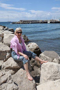 Taş plajda çıplak ayakla oturan bir kadın..