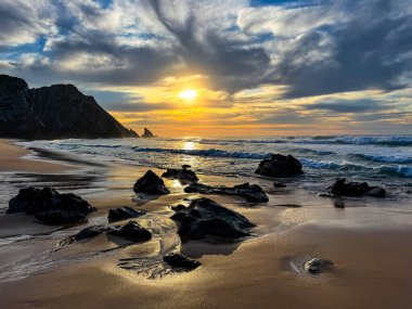 Kum Sahil ve Kaya Sahil Tarifi: Portekiz kıyı şeridi boyunca batan güneşin ılık parıltısıyla yıkanan altın kumlar ve kayalık kayalarla dolu sakin bir sahil.