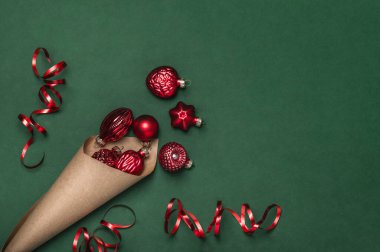 Yeşil arka planda kırmızı oyuncaklarla dolu bir kağıt külah. Yaratıcı Noel arkaplanı, tebrik kartı.