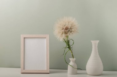 Boş fotoğraf çerçevesi ve içinde karahindiba ve boş vazo olan beyaz vazo. Minimalist iç mekan.