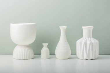 Zeytin duvarına karşı beyaz bir masada dört beyaz seramik vazo..