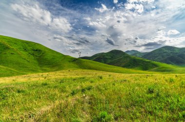 Yeşil tepeler ve yeşil çayırların üzerinde dramatik bulutlu gökyüzü.