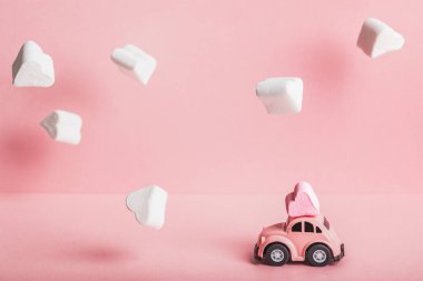Küçük pembe bir araba modeli pembe arka planda lokum bulutlarında kalp şeklinde şekerlemeler taşıyor. Sevgililer Günü, Doğum günü, Düğün Günü, Anneler Günü kavramı.