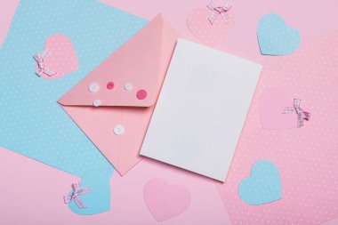 Üzerinde pembe düğmeler, boş kart ve pembe mavi arka planda kağıt kalpler olan pembe bir zarf. Sevgililer Günü konsepti.
