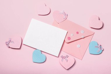 Üzerinde pembe düğmeler, boş kartlar ve pembe arka planda kağıt kalpler olan pembe bir zarf. Sevgililer Günü konsepti.