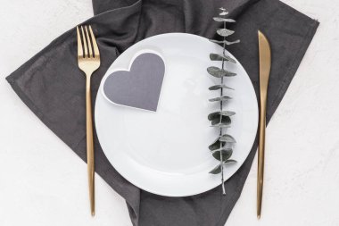 Üzerinde okaliptüs filizi olan gri bir peçete ve kalp şeklinde bir kart. Tebrik kartı, davet, düzen.