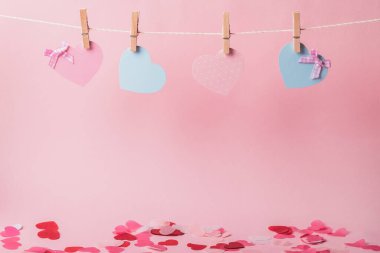 Pembe arka plandaki mandallar üzerinde kağıt pembe ve mavi kalpler. Tatildeyiz. Boşluğu kopyala.