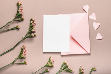 Pembe zarf ve boş form, kahverengi arka planda pembe çiçekler. Kağıt pembe kalpler. Sevgililer Günü için kavram, Anneler Günü.