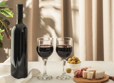 İki kadeh kırmızı şarap ve zeytinli peynir tabağı. Akdeniz mutfağı kavramı.