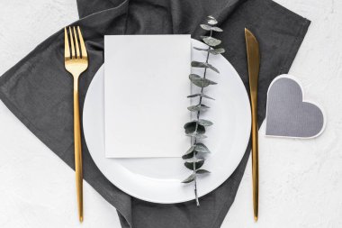 Üzerinde okaliptüs filizi olan gri bir peçeteye beyaz tabak. Tebrik kartı, davetiye, düğün kağıdı boş menü kartı maketi 