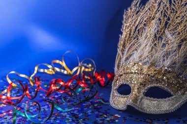 Altın Mardi Gras ya da renkli süslemeli ve konfetili mavi arka planda tüyleri olan karnaval yüz maskesi. Venedik Karnavalı.