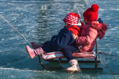 Lake Ara-Kol, Naryn region, Kyrgyzstan - January 5, 2024Two girls in red jackets sled on a frozen lake. Activity during the winter holidays. clipart