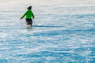 Yeşil ceketli bir çocuk donmuş bir gölde kızağa biniyor. Kış tatillerinde etkinlik.