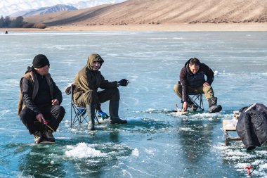 Ara-Kol Gölü, Naryn Bölgesi, Kırgızistan - 5 Ocak 2024: Üç balıkçı donmuş bir gölde balık yakalıyor. Buz balıkçılığı. Kış tatillerinde etkinlik.