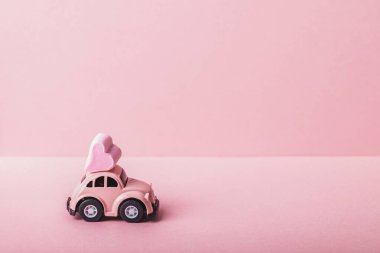 Pembe arka planda kalp şeklinde şekerlemeleri olan küçük pembe bir araba modeli. Sevgililer Günü, Doğum günü, Düğün Günü, Anneler Günü kavramı.