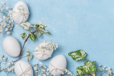 Beyaz Paskalya yumurtaları sicimle süslenmiş ve mavi arka planda çingene dallarıyla süslenmiş. Paskalya kutlaması kavramı. Paskalya arkaplanı..