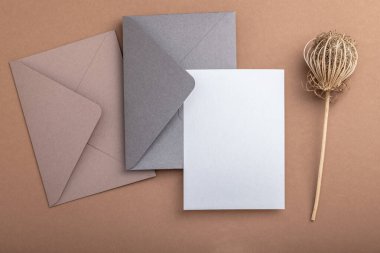 Kahverengimsi arka planda gri bir zarf, boş bir form ve kuru bir çiçek. Sıcak toprak tonları. Tebrik kartı..