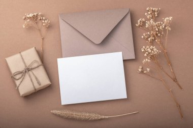 Kahverengi zarf, bej kahve arkaplanı, el işi hediye kutusu ve kurutulmuş çigila çiçekleri. Sıcak toprak tonları. Tebrik kartı..