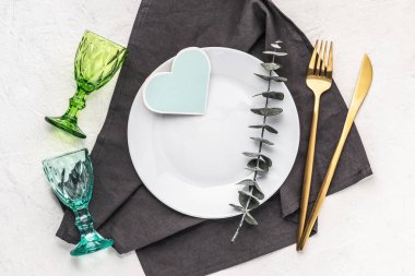 Üzerinde okaliptüs, çatal bıçak, renkli gözlükler ve kalp şeklinde bir kart olan gri bir peçete. Tebrik kartı, davetiye, düğün menüsü modeli.