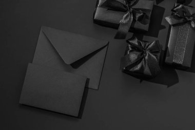 Siyah arka planda saten kurdeleli siyah hediye kutuları ve siyah bir zarf. Tek renkli tebrik kartı..