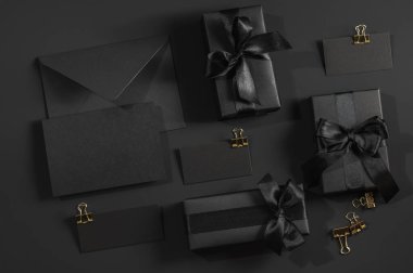 Saten kurdeleli siyah hediye kutuları ve siyah arka plan ve etiketli siyah bir zarf. Tebrik kartı, sertifika.