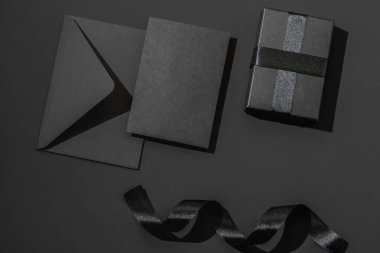 Siyah arka planda siyah bir zarf ve saten kurdeleli siyah hediye kutusu. Tebrik kartı.