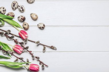 Beyaz ahşap bir masada bıldırcın yumurtaları, söğüt dalları ve pembe laleler. Paskalya arkaplanı.