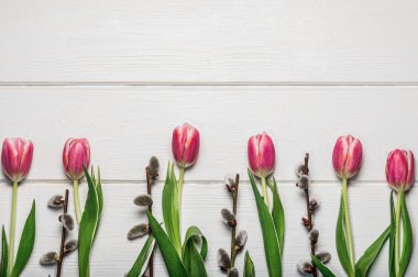 Beyaz ahşap bir masada söğüt dalları ve pembe laleler. Neşeli arkaplan.